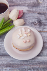 Plate with delicious doughnut with white Crea mIcing, and beautiful Tulip flowers on Rustic grey background with copy space for Text. Vertical image.