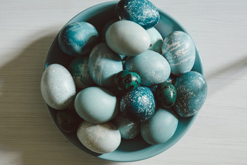 Naturally dyed Easter blue eggs, scattered on blue plate, on white wooden board