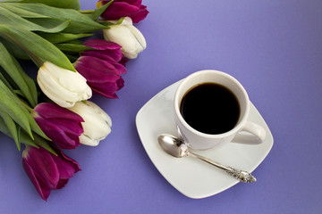 Cup of coffee and tulips on the violet background.Top view.