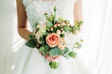 A bride in a white dress is holding a beautiful wedding bouquet.