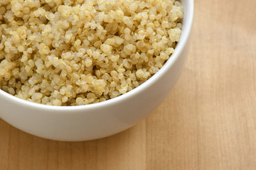 Quinoa in a white bowl on wood cutting board