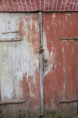 Red barn-door surrounded by a brick wall and damaged, with moss at bottom , photo France, Normandy.