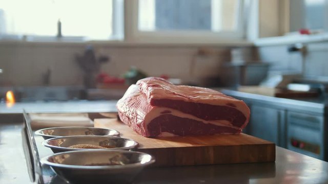 Butcher prepairs large piece of fresh raw meat lying on a wooden board in a commercial kitchen