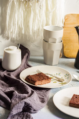 Millet brownie. White plates, cups of coffee and black esspreso maker. White and light blue background. Woolen tapestry.