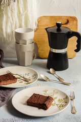 Millet brownie. White plates, cups of coffee and black esspreso maker. White and light blue background. Woolen tapestry.