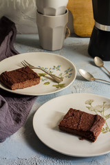 Millet brownie. White plates, cups of coffee and black esspreso maker. White and light blue background. Woolen tapestry.