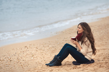 Fototapeta na wymiar Beautiful brunette woman drinking coffee at morning on the beach and enjoying life
