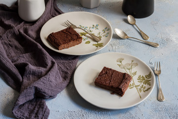 Millet brownie. White plates, cups of coffee and black esspreso maker. White and light blue background. Woolen tapestry.