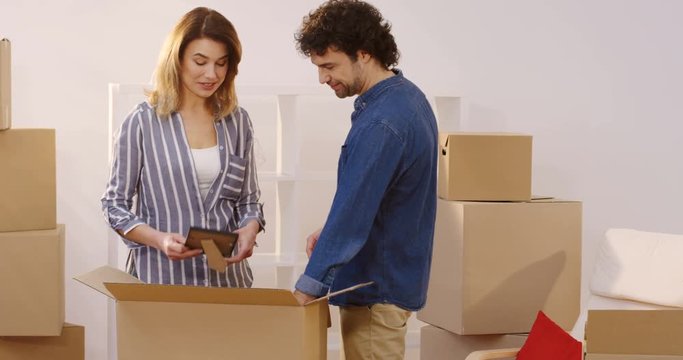 Attractive married man and woman unpacking boxes with different home stuff in their new flat while moving in it. Talking and laughing. Inside