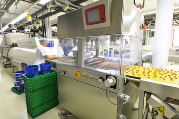 Arbeiter am Fliessband mit Pralinen in einer modernen Fabrik der Lebensmittelindustrie // Worker at...