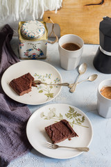 Millet brownie. White plates, cups of coffee and black esspreso maker. White and light blue background. Woolen tapestry.