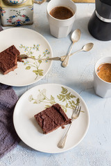 Millet brownie. White plates, cups of coffee and black esspreso maker. White and light blue background. Woolen tapestry.