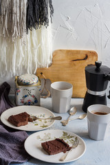Millet brownie. White plates, cups of coffee and black esspreso maker. White and light blue background. Woolen tapestry.