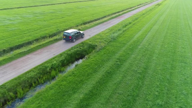 Aerial of unpaved road and off road vehicle following the all wheel car rural area drone view flight backwards away from the SUV beautiful nature and outdoors area typical offroad SUV scene 4k