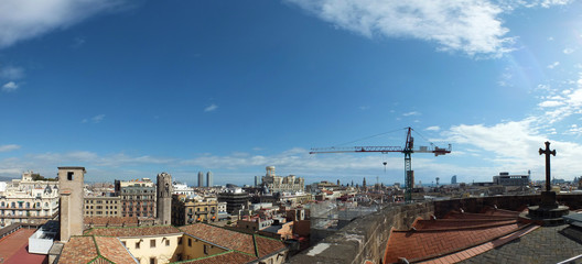 panoramic long image of the city of barcelona showing the roof of the old cathedral with the ancient and modern buildings and skyline extending to the horizon with towers and construction crane