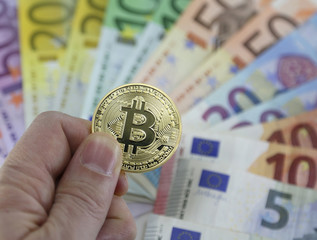 Hand of man with one big goden BITCOIN and euro banknotes on background