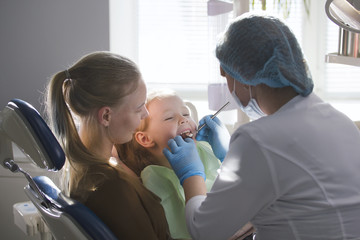 Obraz premium Girl, her mom and the dentist in the dental office, the stomatologist examining and consulting, daughter playing and complaining