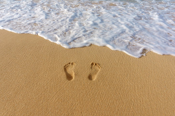 pair of footprints in the sand and sea surf