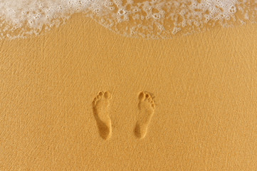 pair of footprints in the sand and sea surf