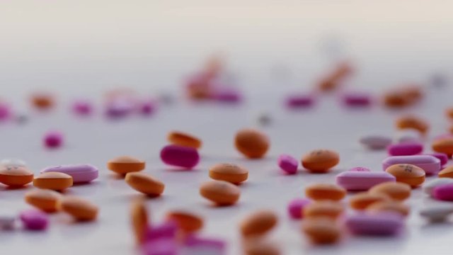 Detail of orange, pink and white tablets falling and bouncing on white surface in soft daylight. Recorded in slow motion HD at 180fps with dolly move.