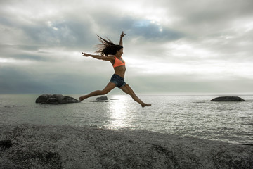 Fototapeta na wymiar Woman jumping on a rock at sunset on Bakovern Beach, Cape Town.