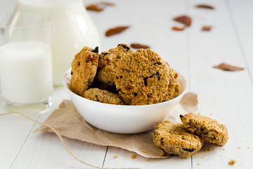 Homemade oatmeal cookies with raisins and prunes with jug and glass of milk on white wooden background. No sugar, no flour, no fast carbs. 
