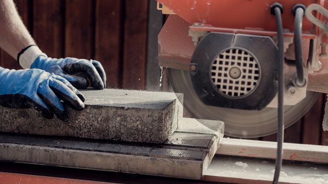 Workman using an angle grinder to cut a concrete block in a side view