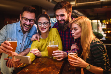 Friends in Pub drinking Beer and Looking at Smartphone