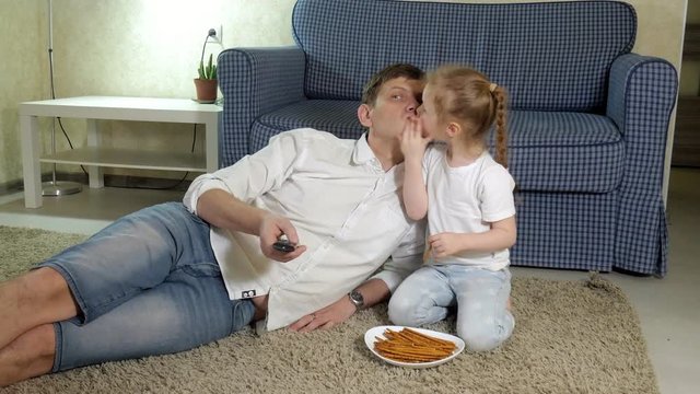 man and daughter watching television, sitting on the floor eating snacks