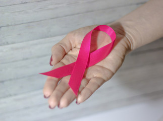 Woman hand giving satin pink ribbon, supporting symbol of breast cancer awareness campaign in October, on light brown paper background with copy space