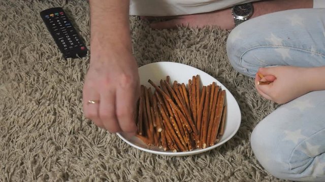 man and daughter watching television, sitting on the floor eating snacks