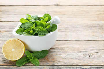 Fresh mint leafs in mortar with lemon on grey wooden table