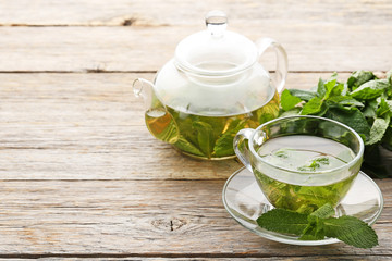 Cup of tea and teapot with mint leafs on wooden table