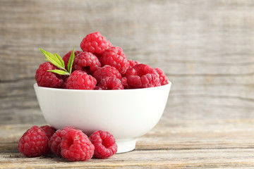 Ripe raspberries in bowl on wooden table