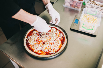 man's hands preparing a pizza before baking, sprinkle cheese on top - 193347980