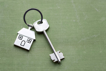 House key and keychain in the form of homes lies on fabric. Concept for real estate, mortgage, moving home or renting property.
