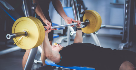 Fototapeta premium Young man lifting the barbell in gym with instructor