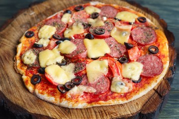 Delicious homemade pizza with salami, olives and tomatoes on chopped wood tray, Italian food