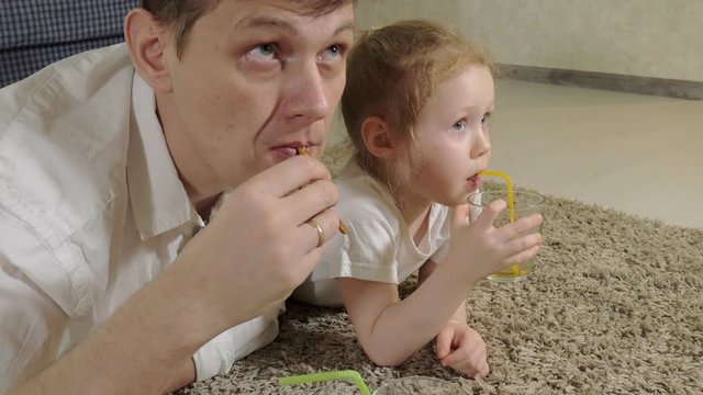 man and daughter watching television, sitting on the floor drink juice