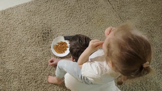 man and daughter watching television, sitting on the floor eating snacks