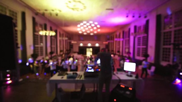 Defocused rear view of music DJ mixing dancing in front his turntables and mixer and laptop during party wedding - illumination with laser light his back large room with guests time lapse
