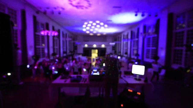Defocused rear view of music DJ mixing dancing in front his turntables and mixer and laptop during party wedding - illumination laser light of his back large room macarena dancing guests