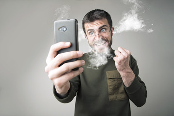Angry man shouting at his cell phone, enraged with the bad service, burning with rage