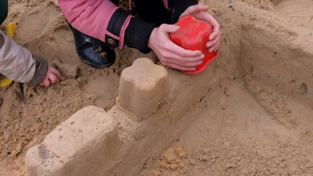 Girl playing with sand on the yard. Construction of a sand castle
 