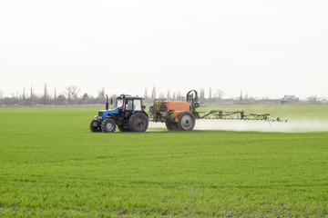 Tractor with high wheels is making fertilizer on young wheat. The use of finely dispersed spray chemicals. Tractor with a spray device for finely dispersed fertilizer.