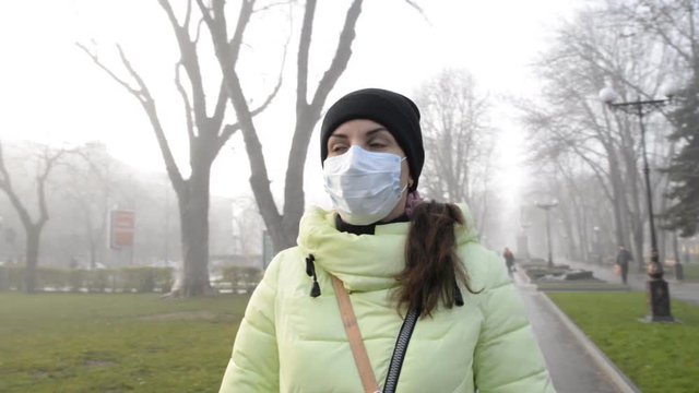 young woman standing on city street in protective medical mask in autumn