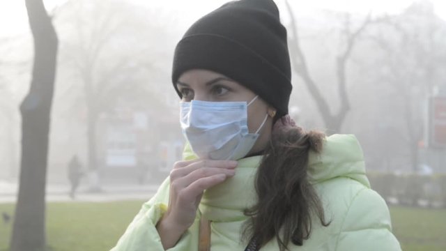 young woman standing on city street in protective medical mask in autumn