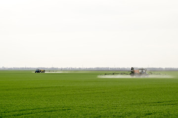 Tractor with high wheels is making fertilizer on young wheat. The use of finely dispersed spray chemicals. Tractor with a spray device for finely dispersed fertilizer.