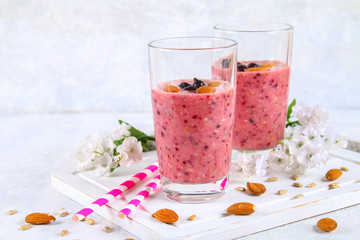Blueberry smoothies of berries, banana and almonds in glasses with cocktail tubes on a white wooden board.