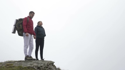 Accomplishment concept with sportive couple in love raising hands cheering and kissing on reaching the mountain peak enjoying the view